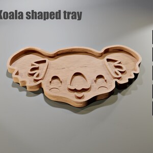 May include: A wooden koala-shaped tray with a smiling face and detailed features. The tray is light brown and has a smooth finish. The text "Koala shaped tray" is at the top. Digital file formats are shown on the right.