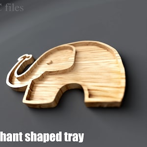 May include: A wooden elephant-shaped tray with a carved design. The tray is made of light-colored wood and features a detailed outline of an elephant. The text "Elephant shaped tray" is at the bottom. The image also includes file type icons.