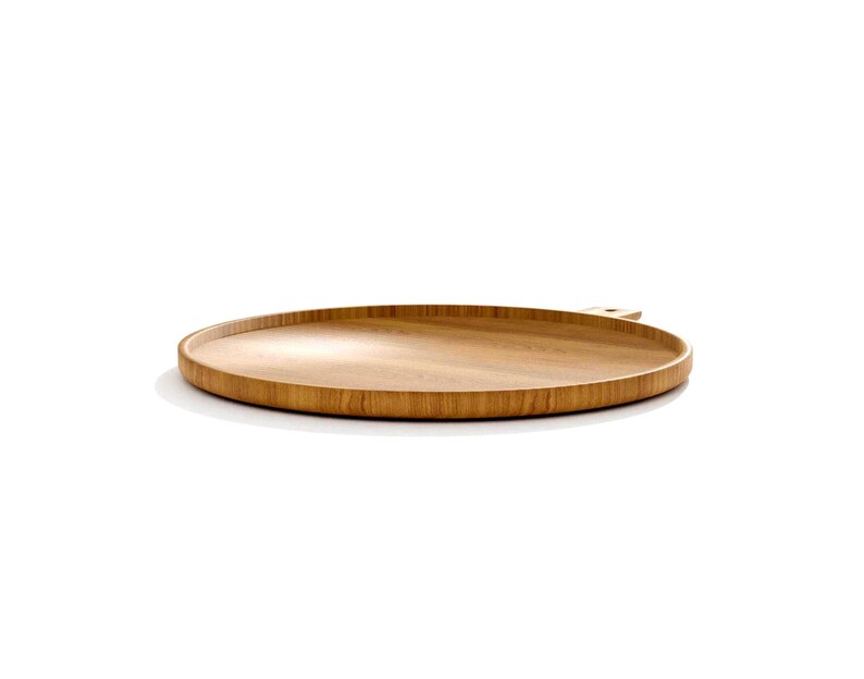 May include: A round, wooden serving tray with a natural wood grain finish. The tray has a slightly raised edge and a small handle. The tray is made of light brown wood and is set against a white background.