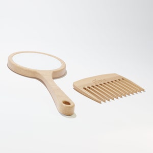 A round wooden hand mirror on the left and a wooden comb on the right