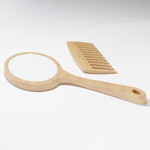 A round wooden hand mirror on the left and a wooden comb on the right