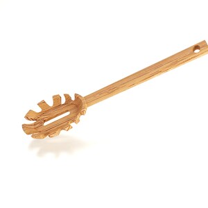 Puede incluir: Un servidor de pasta de madera con un mango largo y un dise&ntilde;o &uacute;nico y dentado. El servidor est&aacute; hecho de madera natural y tiene un color marr&oacute;n claro.
