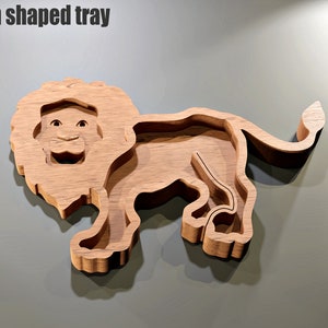May include: A wooden lion-shaped tray with a carved design. The tray is light brown and features a detailed lion face and body. The text "Lion shaped tray" is at the top. The tray is designed with a recessed area for holding items.