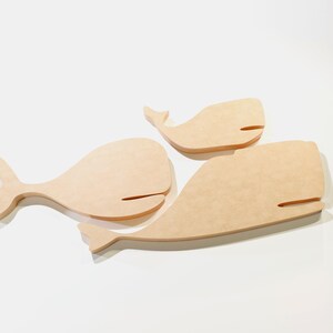 Puede incluir: Tres recortes de ballenas de madera de diferentes tama&ntilde;os. Las ballenas son de color marr&oacute;n claro con un acabado liso y presentan un dise&ntilde;o simple y estilizado. Cada ballena tiene un cuerpo curvo, una cola y una peque&ntilde;a abertura horizontal para la boca.