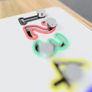 May include: A white wooden board featuring the numbers 1, 2, 3, and 4, each outlined in a different colour: red, green, and yellow. Silver pegs are positioned near each number. The board is framed with wood.