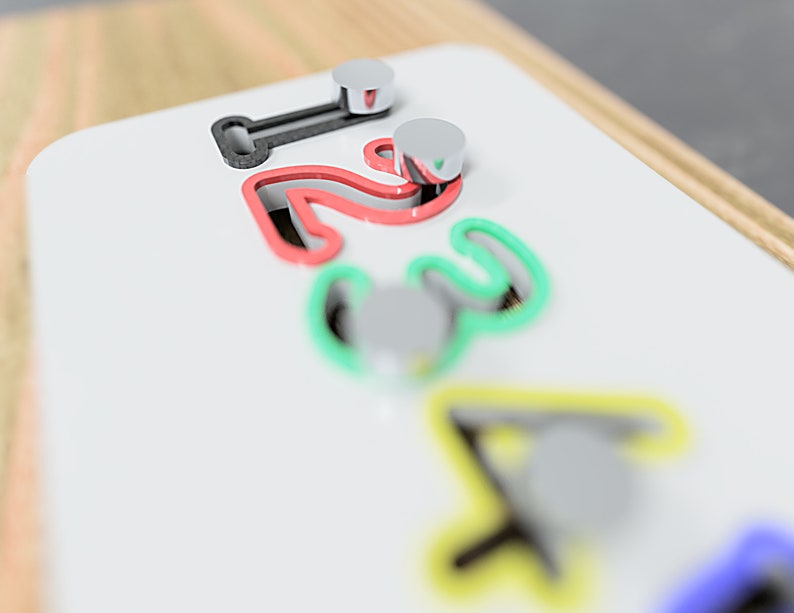 May include: A white wooden board featuring the numbers 1, 2, 3, and 4, each outlined in a different colour: red, green, and yellow. Silver pegs are positioned near each number. The board is framed with wood.