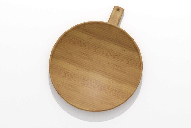 May include: A round wooden serving board with a handle. The board is made of light brown wood and has a natural wood grain pattern. The handle is rectangular and has a hole for hanging. The board is approximately 12 inches in diameter.