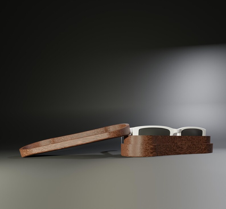 May include: Sunglasses with a white frame and dark lenses rest inside a wooden case. The case is open, with the lid slightly ajar. The case and lid are made of a dark wood.