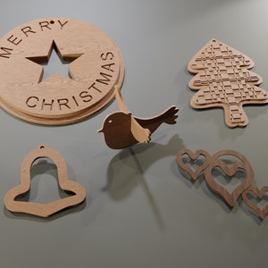 May include: A collection of wooden Christmas ornaments. Includes a round ornament with "MERRY CHRISTMAS" and a star cutout, a bird, a Christmas tree, a bell, and three hearts. All ornaments are made of light brown wood.