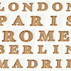 May include: Wooden letters spelling out the names of cities: London, Paris, Rome, Berlin, and Madrid. The letters are a light brown color with a wood grain texture, and are arranged on a white background.