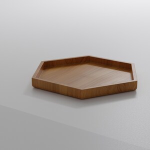 May include: A hexagonal wooden tray with a light brown finish. The tray has a shallow, recessed interior and a smooth, polished surface. The tray is made of wood and is suitable for serving or displaying items.