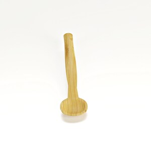 May include: A small, wooden spoon with a rounded bowl and a long, slender handle. The spoon is made of natural bamboo and has a light brown color.