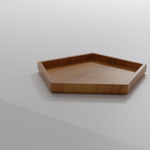 May include: A pentagon-shaped wooden tray with a light brown finish. The tray has a raised edge and a flat interior surface. The wood grain is visible on the surface. The tray is likely used for serving or displaying items.