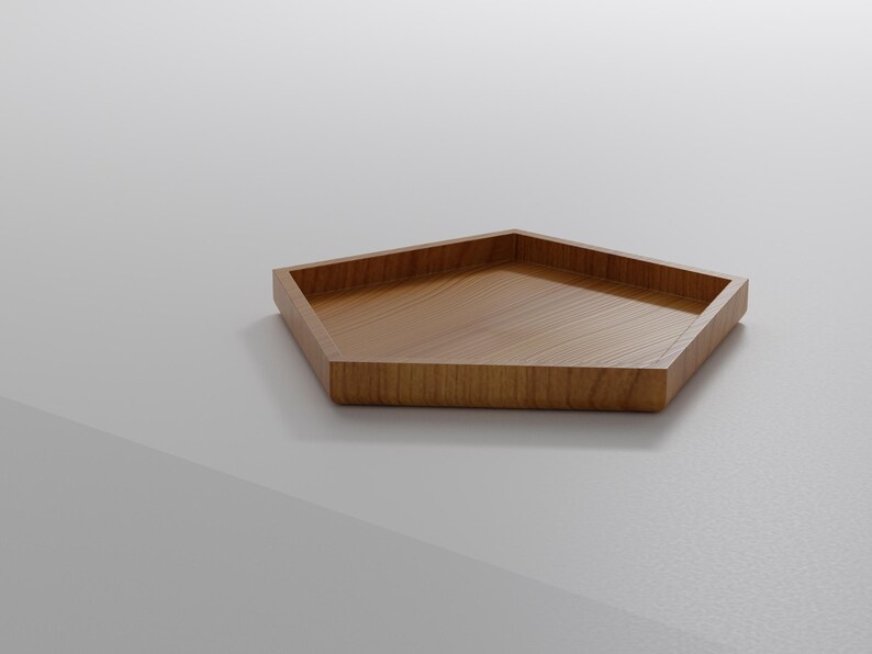 May include: A pentagon-shaped wooden tray with a light brown finish. The tray has a raised edge and a flat interior surface. The wood grain is visible on the surface. The tray is likely used for serving or displaying items.