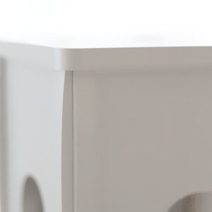 May include: A close-up of a white, rectangular, wooden structure with rounded holes. The structure has a flat top and is painted in a solid, neutral white color. The background is blurred, suggesting a bright, natural light source.