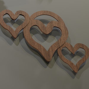 May include: Three wooden heart-shaped wall decorations. The hearts are cut from a light brown wood and are arranged in a cluster. The wall behind the hearts is a solid gray color. The hearts are casting shadows.