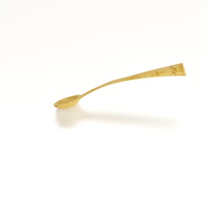 May include: A gold-colored metal spoon with a rounded bowl and a long, slender handle.