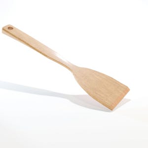 May include: A light-colored wooden spatula with a flat, rectangular head and a long, slender handle. The handle has a small hole at the end for hanging. The spatula is made of a light-colored wood and is designed for cooking and food preparation.