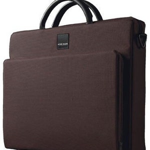 May include: A brown canvas laptop bag with a black leather handle and a black strap. The bag has a zippered closure and a small pocket on the front with the text "AIME MADE" printed on it.