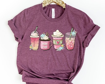 Pode incluir: Uma camiseta vinho com um gráfico de quatro bebidas de café diferentes. As bebidas são decoradas com chantilly, granulado e canudos. O texto "Mom Fun" está impresso na camiseta.