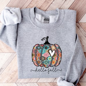 Puede incluir: Una sudadera gris con una calabaza estampada de colores y el texto "hello fall" impreso en la parte delantera.