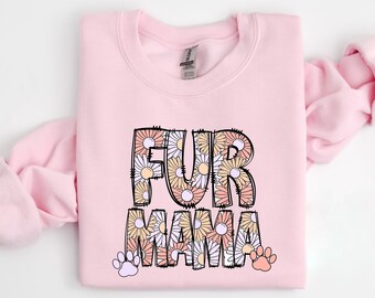 Könnte beinhalten: Rosafarbener Pullover mit dem Text "FUR MAMA" in schwarz umrandeten Buchstaben, die mit einem Blumenmuster gefüllt sind. Die Buchstaben sind von zwei Pfotenabdrücken umgeben.