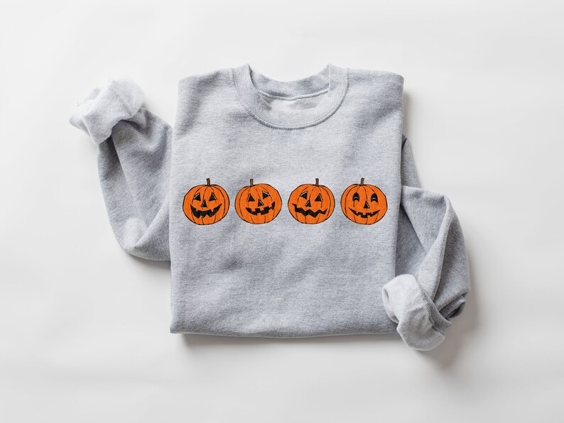 May include: A gray sweatshirt with a row of four orange jack-o'-lantern pumpkins with different facial expressions.