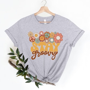 May include: A gray t-shirt with a retro-style graphic design featuring a peace sign, flowers, and the text "Stay Groovy".