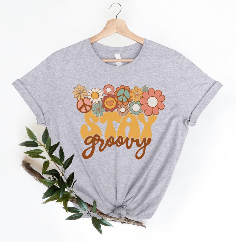 May include: A gray t-shirt with a retro-style graphic design featuring a peace sign, flowers, and the text "Stay Groovy".