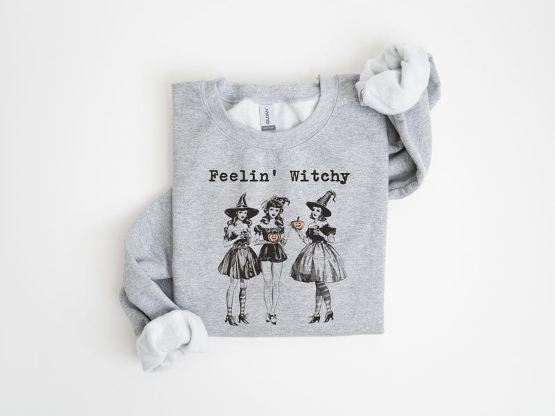 May include: Gray sweatshirt with the text "Feelin' Witchy" and a graphic of three witches in black dresses and pointy hats holding pumpkins.