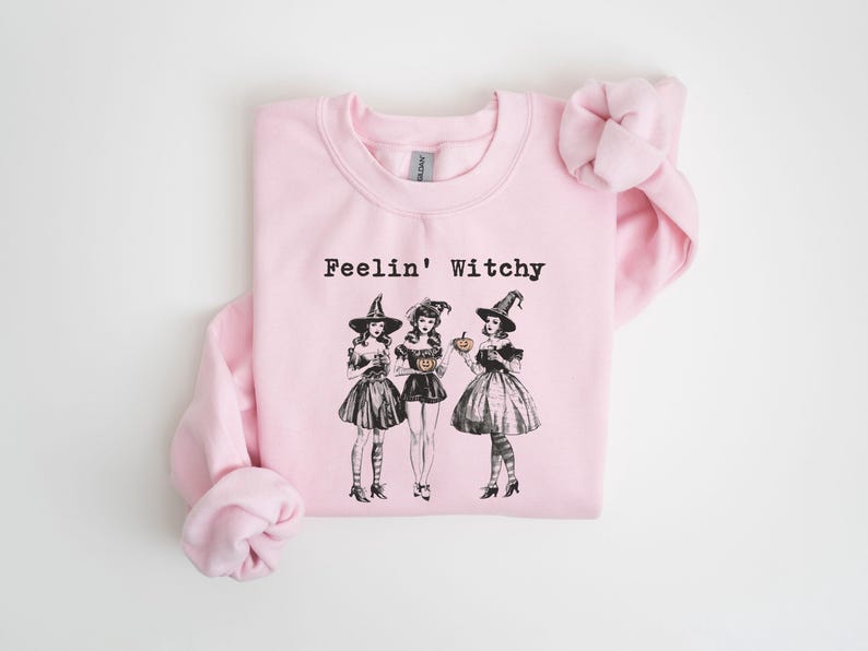 May include: Pink sweatshirt with the text "Feelin' Witchy" and a graphic of three witches in black dresses and pointy hats holding pumpkins.