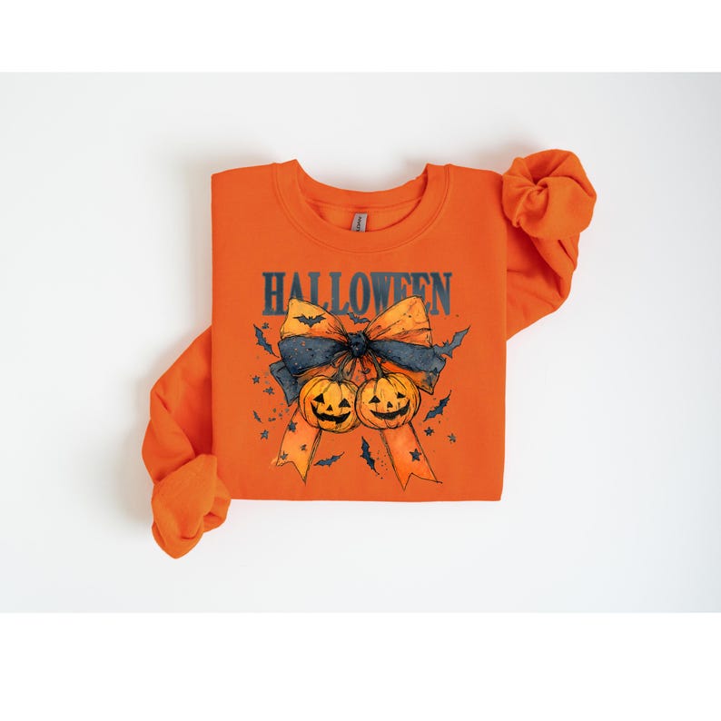 Puede incluir: Sudadera naranja con un dise&ntilde;o de Halloween. El dise&ntilde;o presenta un lazo, dos calabazas talladas, murci&eacute;lagos y la palabra "HALLOWEEN" en azul oscuro. La sudadera tiene mangas largas.