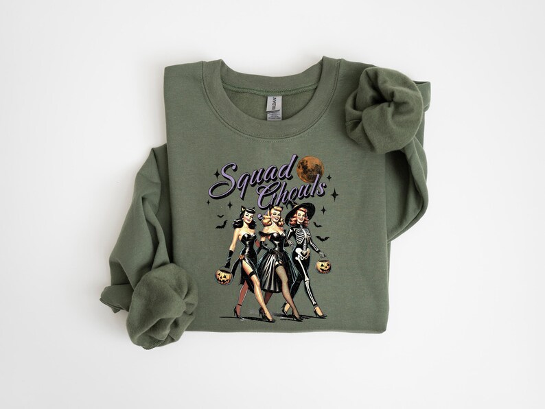 May include: Green sweatshirt with a graphic of three women dressed as witches for Halloween. The text "Squad Goals" is printed on the sweatshirt.