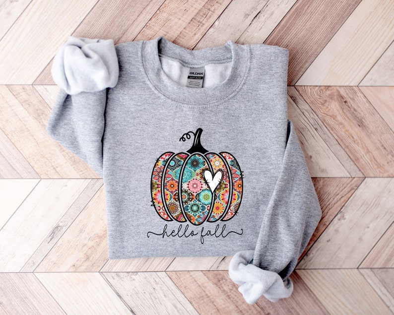 Puede incluir: Una sudadera gris con una calabaza estampada de colores y el texto "hello fall" impreso en la parte delantera.