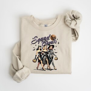 May include: A beige sweatshirt with a graphic print of three women dressed in Halloween costumes. The text "Squad Goals" is printed above the women.