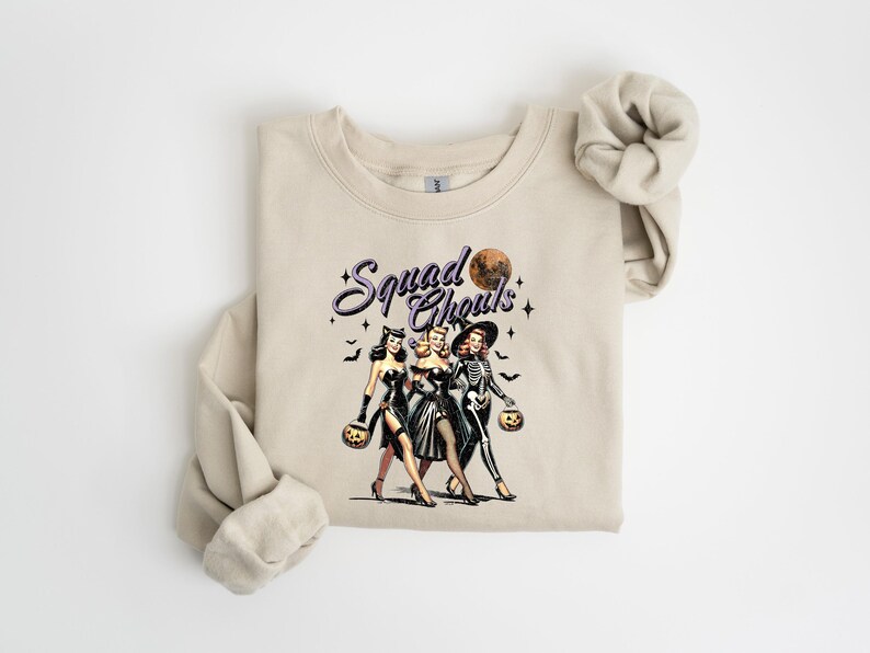 May include: A beige sweatshirt with a graphic print of three women dressed in Halloween costumes. The text "Squad Goals" is printed above the women.