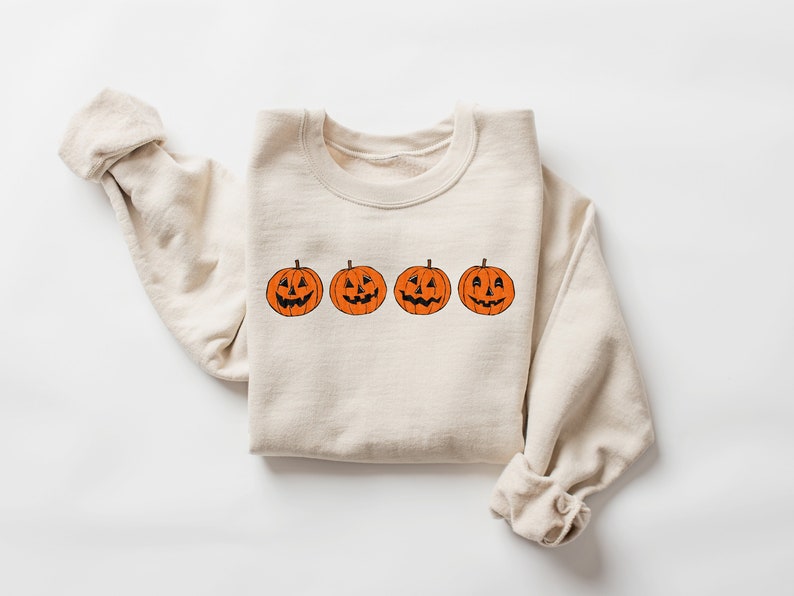 May include: A beige sweatshirt with a row of four orange jack-o'-lantern faces printed on the front.