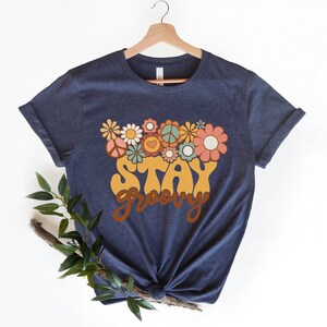 May include: A navy blue t-shirt with a yellow "Stay Groovy" graphic and a floral design in shades of pink, orange, green, and blue.