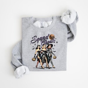 May include: Gray sweatshirt with a vintage-style illustration of three women dressed as witches and a skeleton holding jack-o-lanterns. The text "Squad Goals" is printed above the illustration.