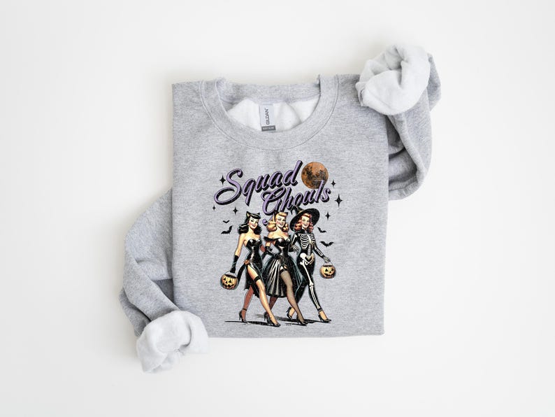 May include: Gray sweatshirt with a vintage-style illustration of three women dressed as witches and a skeleton holding jack-o-lanterns. The text "Squad Goals" is printed above the illustration.
