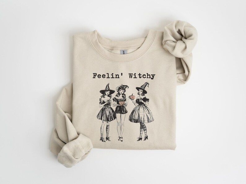 May include: A beige sweatshirt with the text "Feelin' Witchy" and a graphic of three witches holding pumpkins.