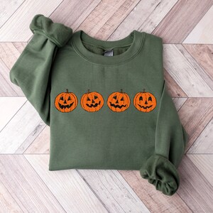 May include: A green sweatshirt with a row of four orange jack-o'-lantern pumpkins with black eyes, noses, and mouths.