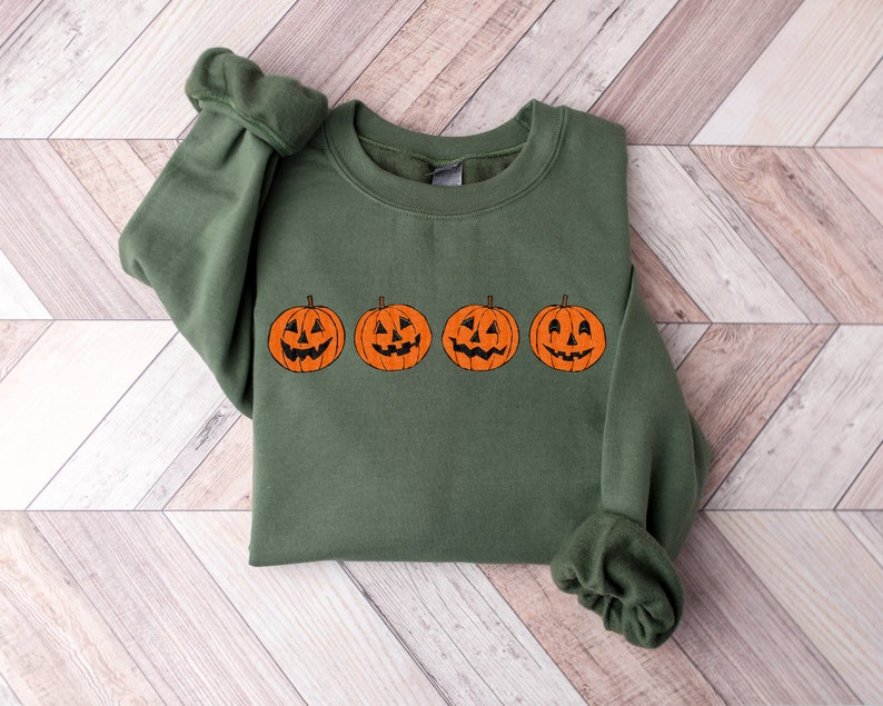 May include: A green sweatshirt with a row of four orange jack-o'-lantern pumpkins with black eyes, noses, and mouths.