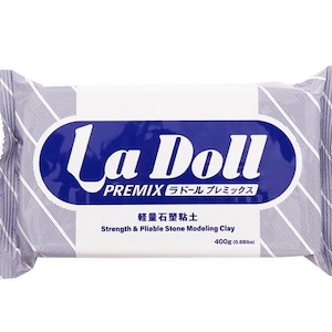 Op de afbeelding: Een verpakking La Doll Premix boetseerklei. De verpakking is wit met blauwe diagonale strepen en een blauwe ovaal met de merknaam. Tekst op de verpakking luidt "Strength & Pliable Stone Modeling Clay" en "400g".