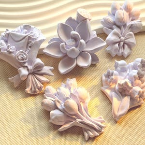 Op de afbeelding: Vijf licht lavendelkleurige decoratieve ornamenten met bloemmotieven. De collectie bevat een boeket met een envelop, een lotusbloem, een tulpentros met een strik, een cluster van kleine knoppen en een gedetailleerd bloemstuk.