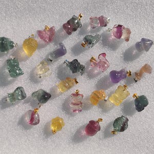 Puede incluir: Una colección de colgantes de piedras preciosas talladas y coloridas, con diversos diseños inspirados en animales y la naturaleza. Los colgantes están hechos de fluorita, amatista y otras piedras semipreciosas.