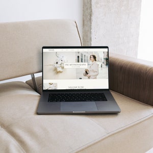 K&ouml;nnte beinhalten: Ein Laptop-Computer, auf dem eine Website f&uuml;r Fine-Art-Fotografie angezeigt wird. Die Website zeigt eine wei&szlig;e Blumenarrangements und eine Frau in einem wei&szlig;en Mantel und einem Hut.