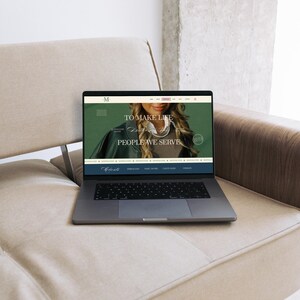 May include: A laptop displaying a website with the text "TO MAKE LIFE PEOPLE WE SERVE" sits on a beige sofa. The laptop is open, showing a website with a woman's image. The sofa is light beige, and the background is a neutral color.