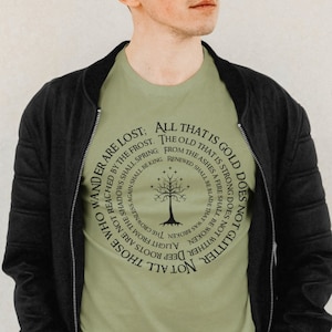 May include: A green t-shirt with a black circular design featuring a tree with stars and the text "All that is gold does not glitter, not all those who wander are lost: The old that is strong does not wither, deep roots are not reached by the frost. From the ashes a fire shall be woken, a light from the shadows shall spring, renewed shall be blade that was broken, the crownless shall be king."