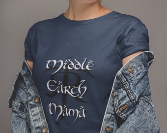May include: A woman wearing a blue denim jacket over a navy blue t-shirt with the text "Middle Earth" in black script. She is wearing a blue and white patterned head scarf.